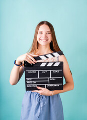 Happy smiling teenager girl in a blue dress holding a clapper board isolated on blue