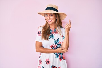 Middle age hispanic woman wearing summer hat smiling happy pointing with hand and finger to the side