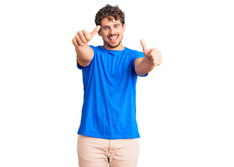 Young handsome man with curly hair wearing casual clothes approving doing positive gesture with hand, thumbs up smiling and happy for success. winner gesture.