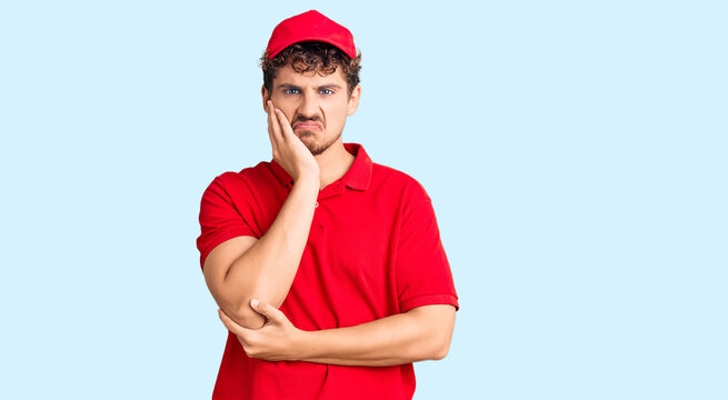 Young handsome man with curly hair wearing delivery uniform thinking looking tired and bored with depression problems with crossed arms.