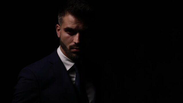dramatic elegant fashion model in suit touching lips and posing in a fashion light, crossing arms and moving, looking to side and standing on dark background