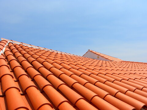 Red tile roof under blue sky. The photo is divided in half. One part is a roof made of clay tiles and the other is a pure blue sky.