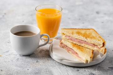 Ham and cheese sandwich, cup of coffee with milk and orange juice glass on concrete table in coffee shop at the morning. Typical breakfast in many countries.
