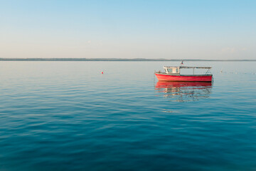 Small red fishing boat stands on blue clear water in the sea.