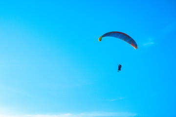 Doubles paragliding against a clear blue sky. A multi-colored papaplan flies in the clear sky closeup.