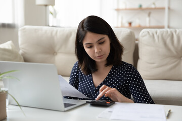 Concentrated Asian young woman work on laptop mange household finances expenditures, focused Vietnamese millennial girl use computer, calculate home utility expenses, pay bills taxes online