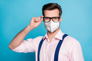 Close-up portrait of his he nice attractive healthy guy wearing respirator safety mask touching specs stop respiratory disease china wuhan syndrome isolated bright vivid blue color background