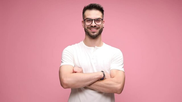 handsome casual man wearing eyeglasses, standing against pink background, crossing his arms to chest and smiling