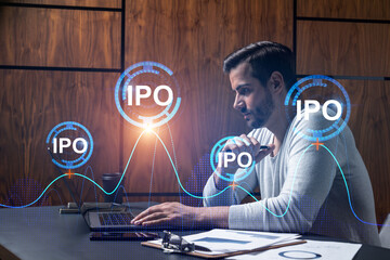 A serious caucasian analyst in casual wears, using laptop to analyze the profit of IPO project. Double exposure. Initial public offering Hologram. Concept of a growth of investments.
