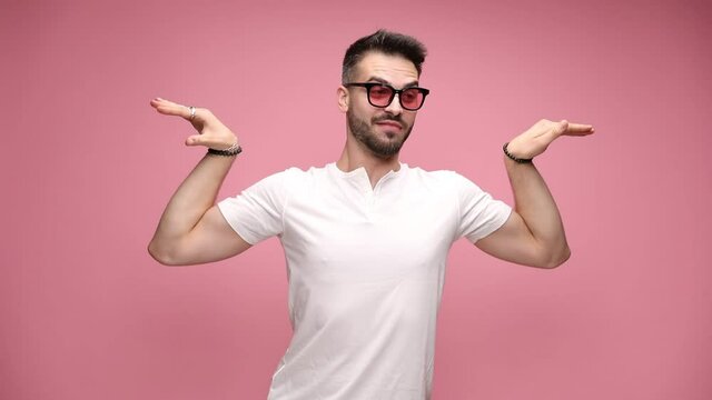 young handsome casual guy posing like a bodybuilder, flexing his arms, waving his hands, fading out and laughing on pink background