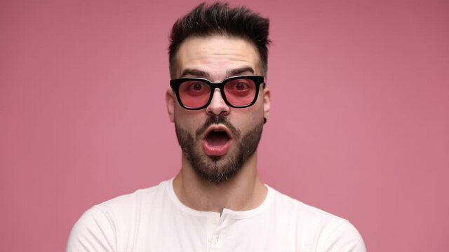 close up of a casual man looking at camera, being serious then adopting a fearful expression on his face, being surprised then happily surprised on pink background