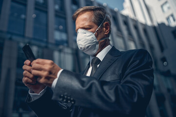 Handsome man in medical face mask using cellphone outdoors