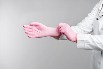 Female doctor's hands putting on pink sterile gloves isolated on gray background