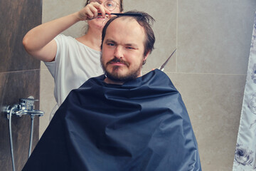 Fototapeta premium Haircut and hairstyle at home, man and woman in the bathroom. Concept of recovery and return to normal life after the coronavirus epidemic