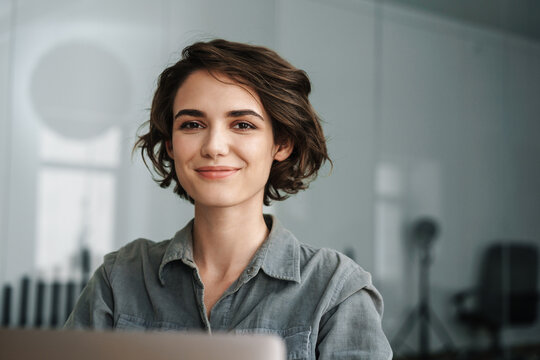 Image of young beautiful joyful woman smiling while working with laptop