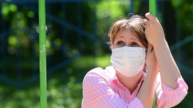 A young woman sitting in a Park on a swing suffers from heat. A woman in a Park takes off her mask and puts it on.