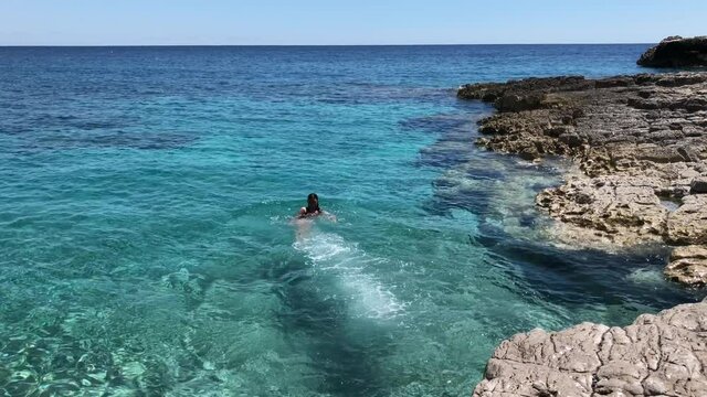 Brave young woman jumping off a cliff into the clear sea bay. Sunny day, no people, blue sea to the horizon