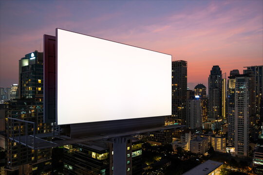 Blank white road billboard with Bangkok cityscape background at night time. Street advertising poster, mock up, 3D rendering. Side view. The concept of marketing communication to sell idea.