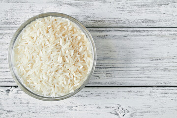 Raw white rice grains in a transparent glass plate on wooden background. Closeup, top view