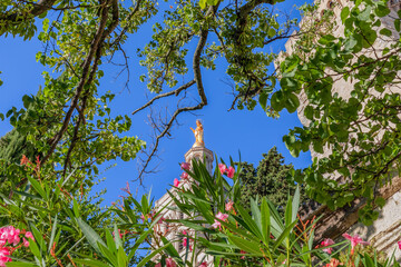 Statue of Golden Virgin Mary surrounded by flowers from the garden at the Palace of the Popes in...