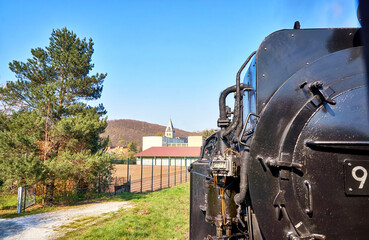 Steam locomotive drives past a sports field with a church tower in the background. Dynamic due to motion blur.