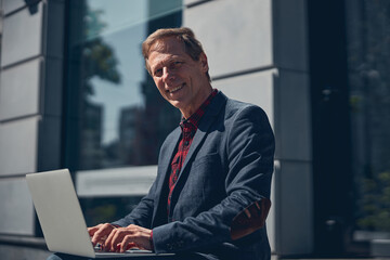 Cheerful man working on modern laptop outdoors