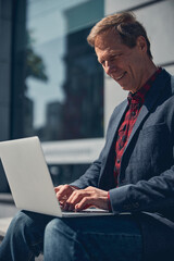 Handsome cheerful man working on notebook on the street