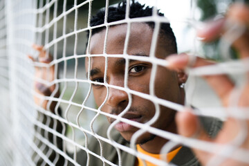 Frustrated young black man behind net outdoors in city, black lives matter concept.