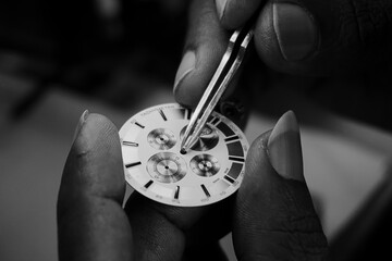 Black and white closeup photograph of a watchmaker examining the dial of a watch under a light...