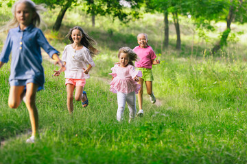 Obraz premium Kids, children running on meadow in summer's sunlight. Look happy, cheerful with sincere bright emotions. Cute caucasian boys and girls. Concept of childhood, happiness, movement, family and summer.