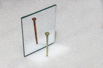 The new nail sees its rusty reflection in the mirror. The concept of the fluidity of time, aging. The main object is a rusty nail in the mirror.