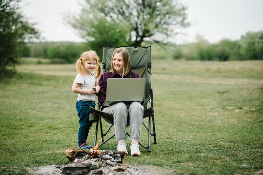 Quarantine, closed nursery school during coronavirus outbreak. Communication with family online on laptop near fire in nature. Homeschooling, freelance job. Mother work on Internet with kid outdoors.