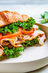 Croissant sandwich with meat, vegetables and green kale, white background. Breakfast food concept.