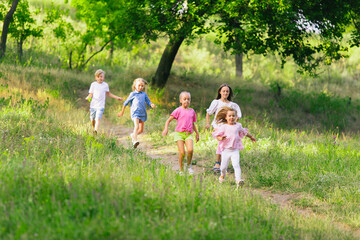 Naklejka premium Kids, children running on meadow in summer's sunlight. Look happy, cheerful with sincere bright emotions. Cute caucasian boys and girls. Concept of childhood, happiness, movement, family and summer.