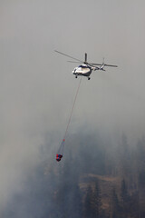 Fototapeta na wymiar Forest fire. Firefighting helicopter lowers water under fire of helicopter and extinguishes huge forest fires. Special helicopter in flight suspension with a fire extinguishing drainage device