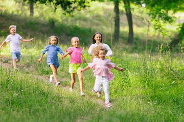 Fototapeta premium Kids, children running on meadow in summer's sunlight. Look happy, cheerful with sincere bright emotions. Cute caucasian boys and girls. Concept of childhood, happiness, movement, family and summer.