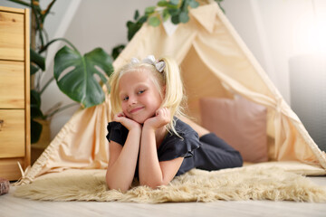 Little girl with a smile in her room on the floor next to the wigwam tent © pridannikov
