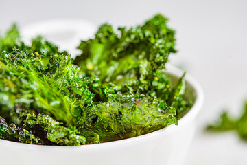 Green kale chips with salt in white bowl. Healthy vegan food concept.