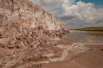 Soligork salt mine slagheap mountains and scenic nature with dramatic cloudy blue sky in summer day. A technical water lake, white salt rock and cracked ground