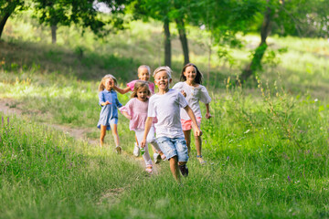 Obraz premium Kids, children running on meadow in summer's sunlight. Look happy, cheerful with sincere bright emotions. Cute caucasian boys and girls. Concept of childhood, happiness, movement, family and summer.