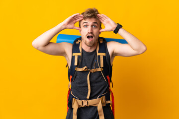 Young mountaineer man with a big backpack isolated on yellow background with surprise expression