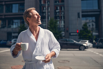 Handsome joyful man in bathrobe standing on the street