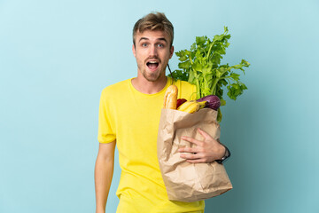 blonde Person taking a bag of takeaway food isolated on blue background with surprise facial...