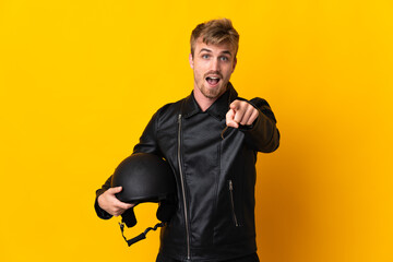 Man with a motorcycle helmet isolated on yellow background surprised and pointing front