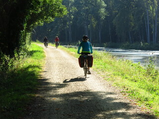 Jeune femme cycliste à vélo avec sacoche sur piste cyclable pour randonnée bicyclette le long d'un canal d'eau de rivière en France dans la Loire