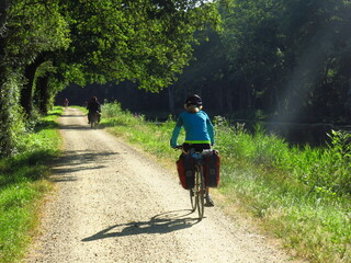 Obraz premium Jeune femme cycliste à vélo avec sacoche sur piste cyclable pour randonnée bicyclette le long d'un canal d'eau de rivière en France dans la Loire