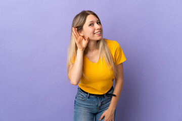 Young blonde woman isolated on purple background listening to something by putting hand on the ear