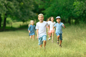 Fototapeta premium Kids, children running on meadow in summer's sunlight. Look happy, cheerful with sincere bright emotions. Cute caucasian boys and girls. Concept of childhood, happiness, movement, family and summer.