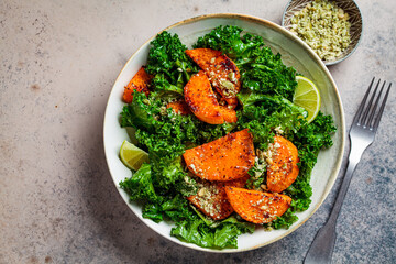 Baked sweet potato salad with kale in white bowl, dark background, top view. Vegan food concept.