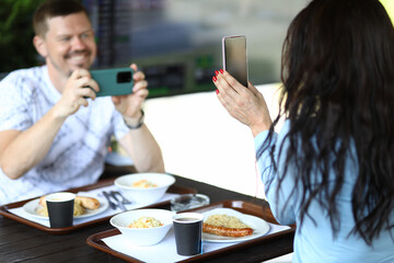 Woman is holding smartphone in her hands, man is filming review of novelty on smartphone in cafe. Tests and video reviews of new concept products